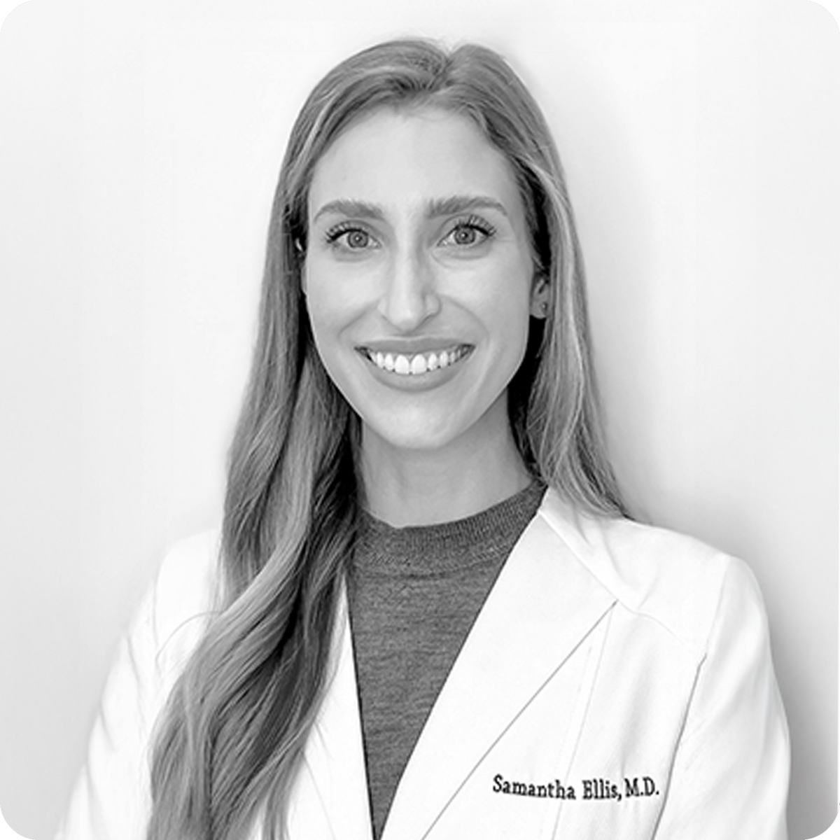 Black and white photo of a woman wearing a white lab coat with 'Samantha Ellis, M.D.' on it.