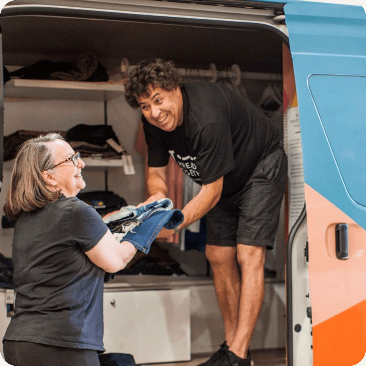 Two people organizing items inside a van with a focus on a blue and orange logo.